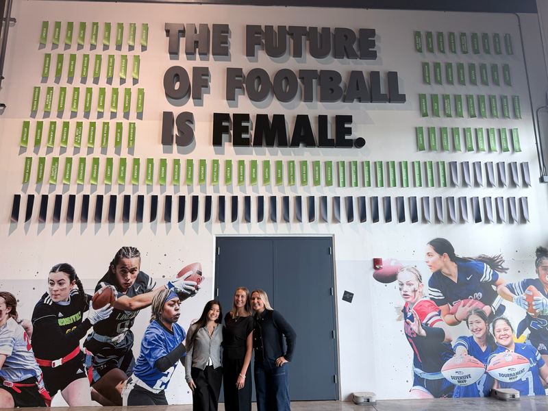 Students at Lumen Field in front of a wall reading the future of football is female.