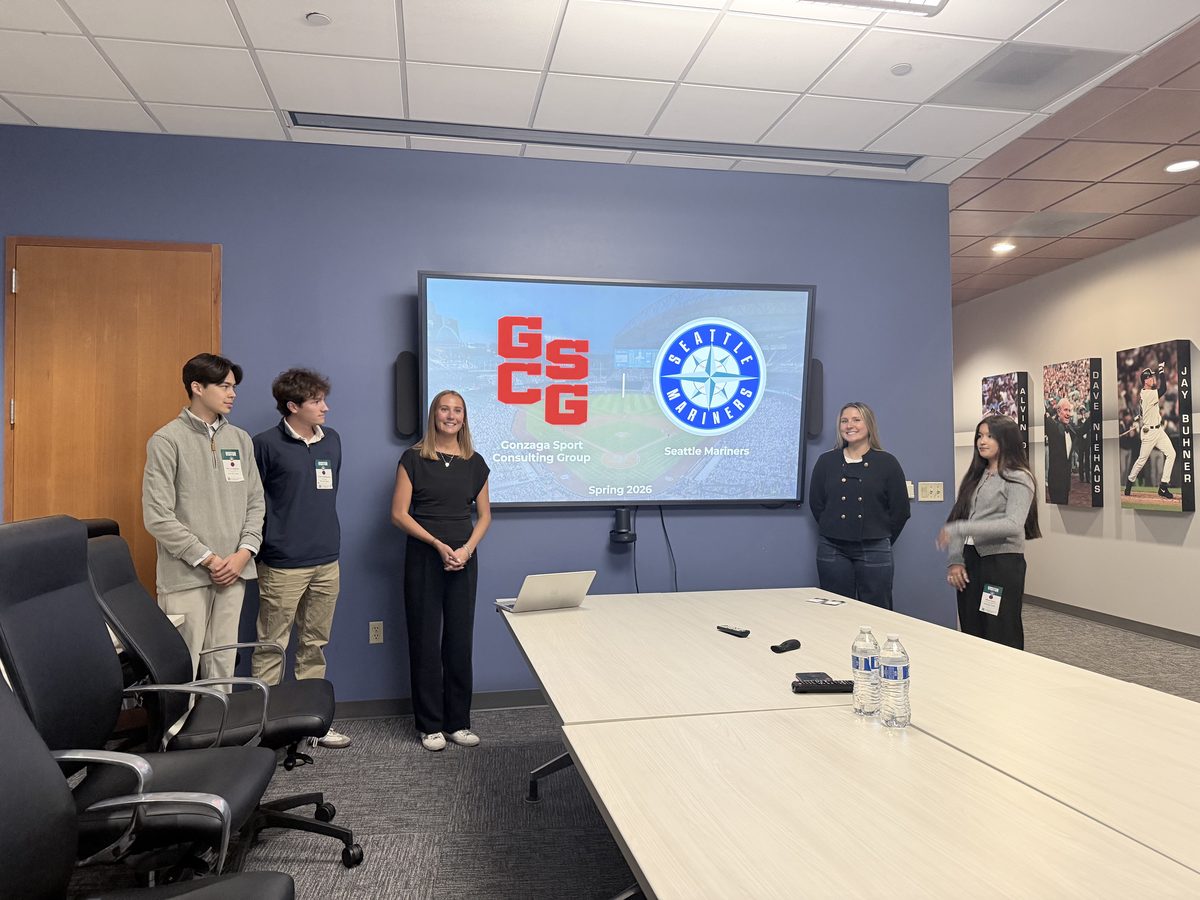 Five Gonzaga Sport Consulting Group students standing beside a screen showing the GSCG and Seattle Mariners logos in a Mariners meeting room.