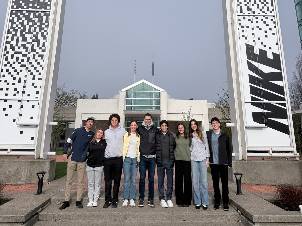 Nine students on the steps at Nike World Headquarters, framed by two Nike banners.